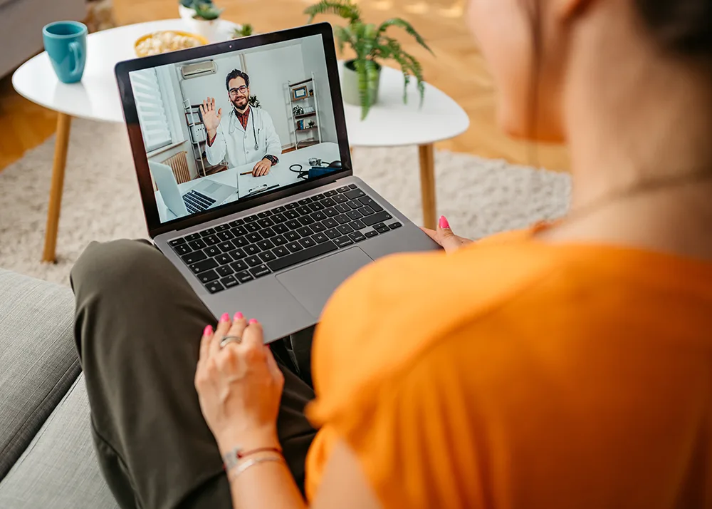 Woman uses a laptop to ask a healthcare professional about ancillary benefits insurance.