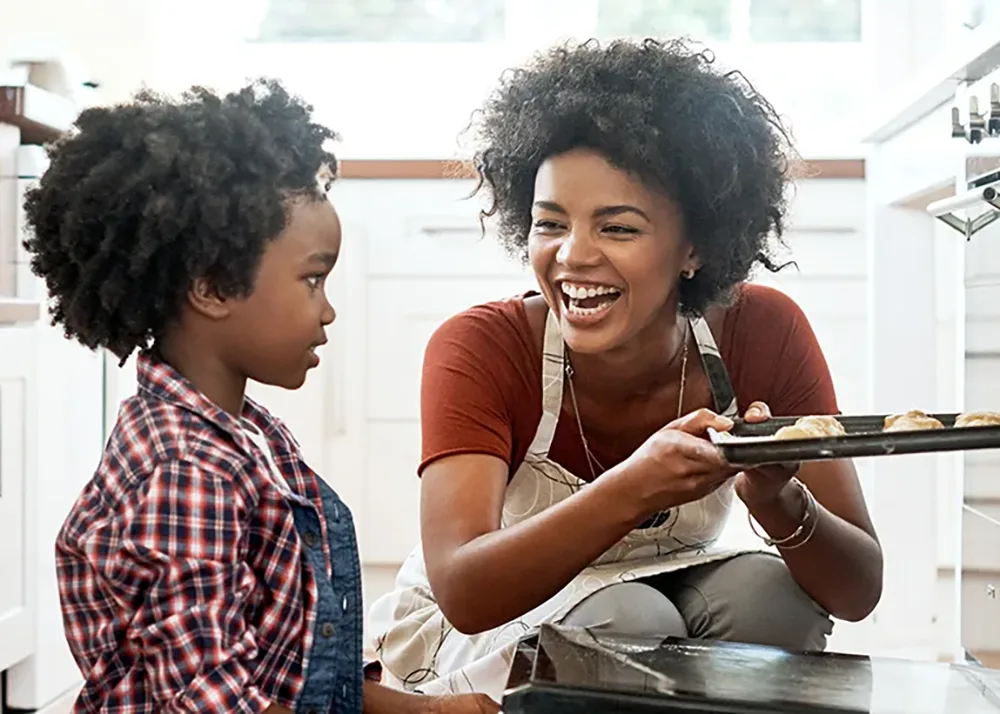 Mother and her child put a tray of cookies into an oven.