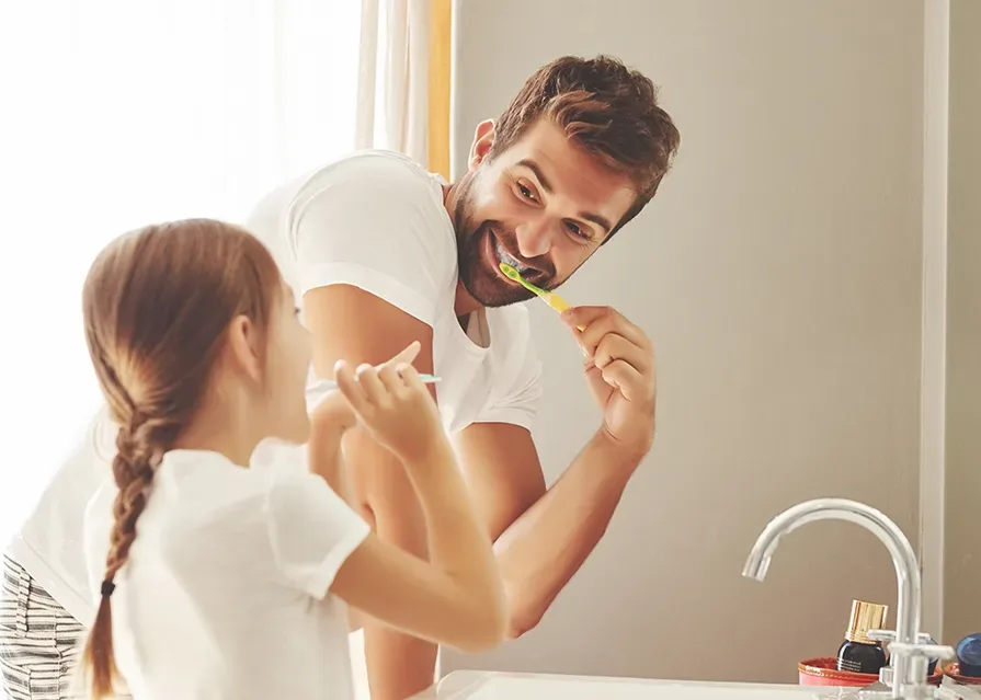 A father and his daughter are brushing their teeth.