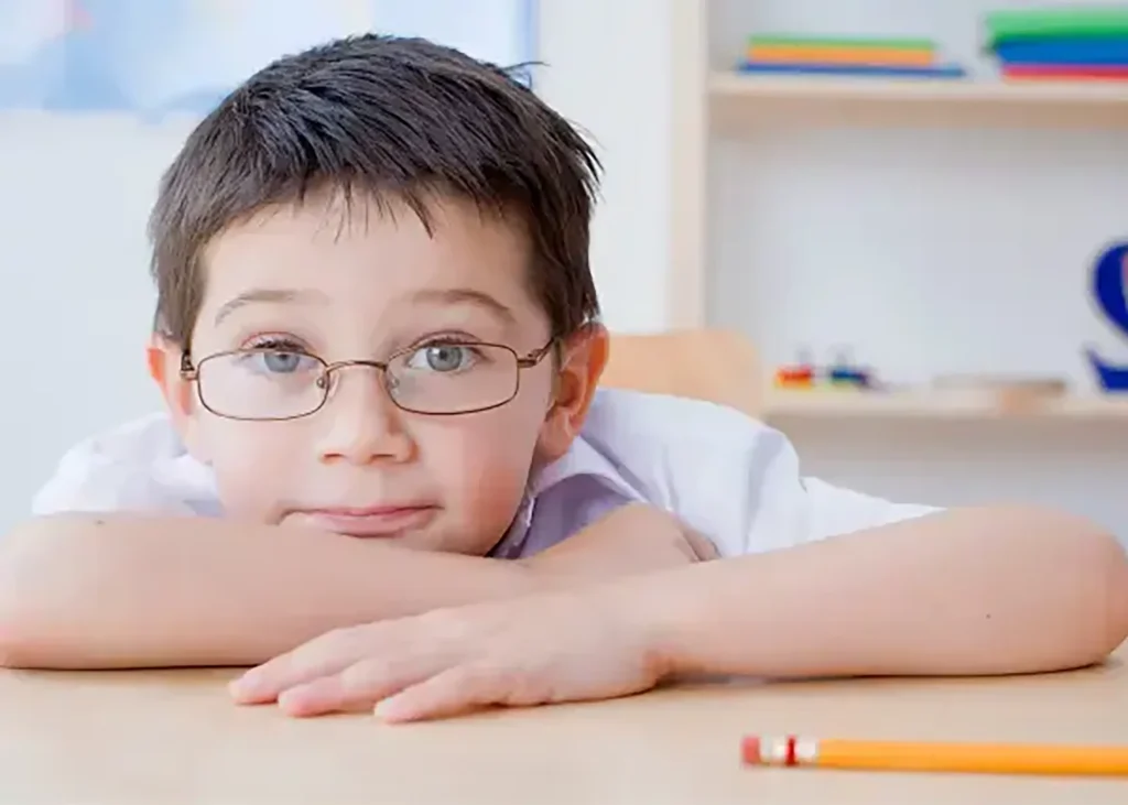 A young boy in glasses sitting at his desk.