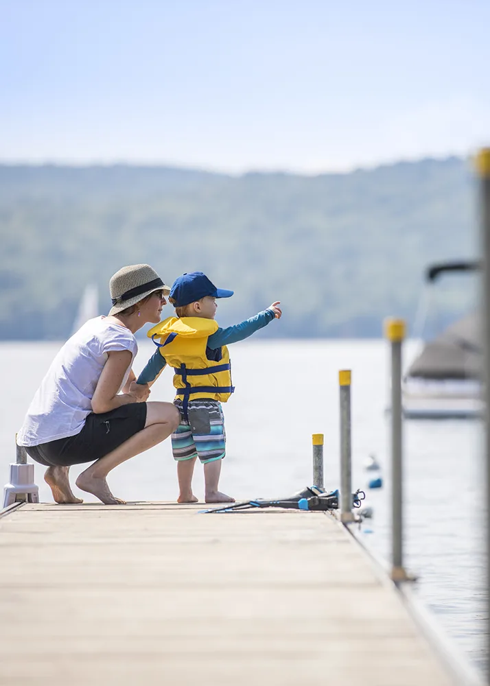 Mother and her toddler in a life vest standing on a pier.