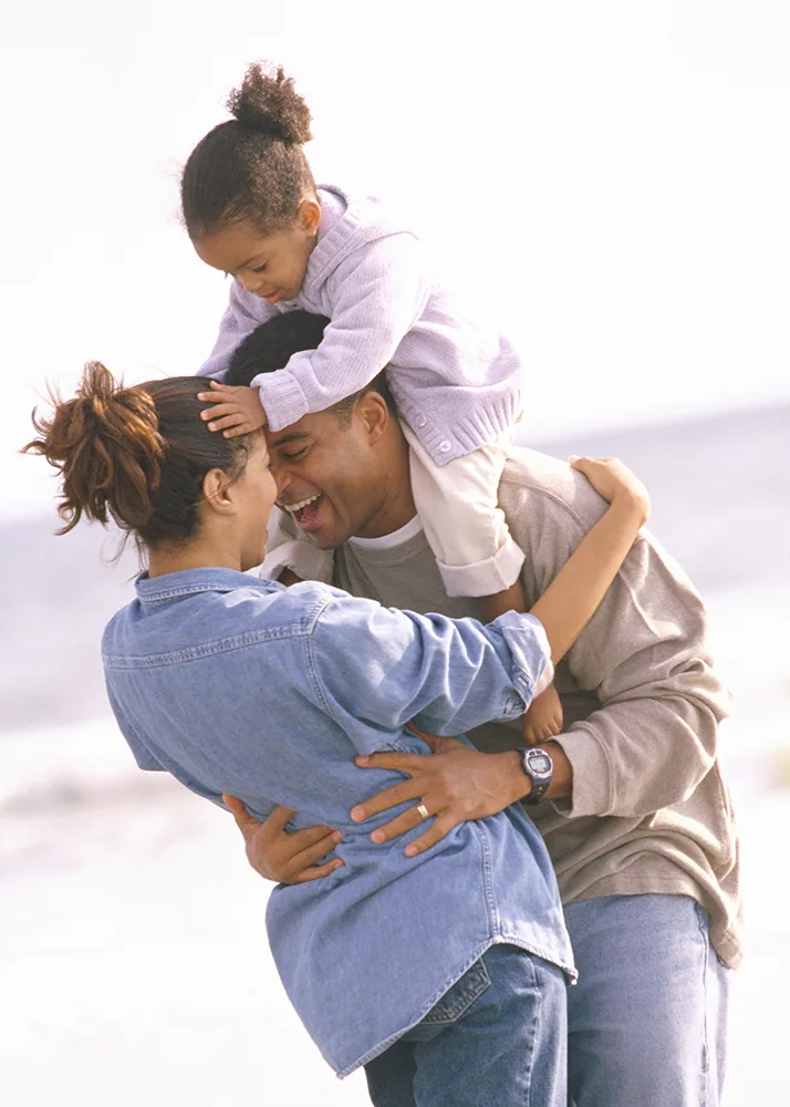 Happy father with his little daughter sitting on his shoulders hugging his wife.