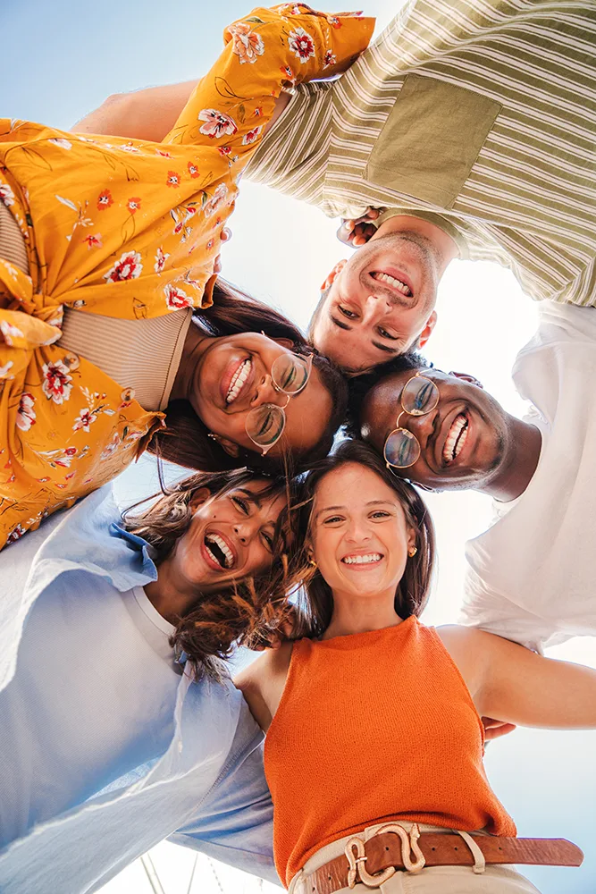 A group of five young people of different races and genders are standing in a circle and looking down at a camera.