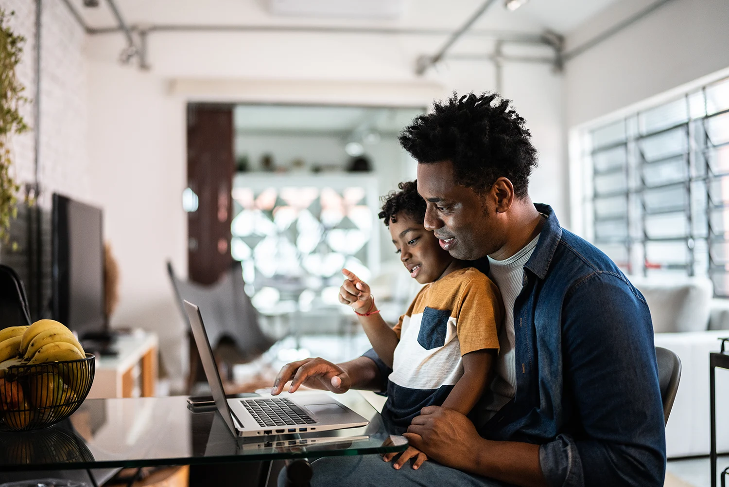 a man and young child look at laptop togther while in kitchen