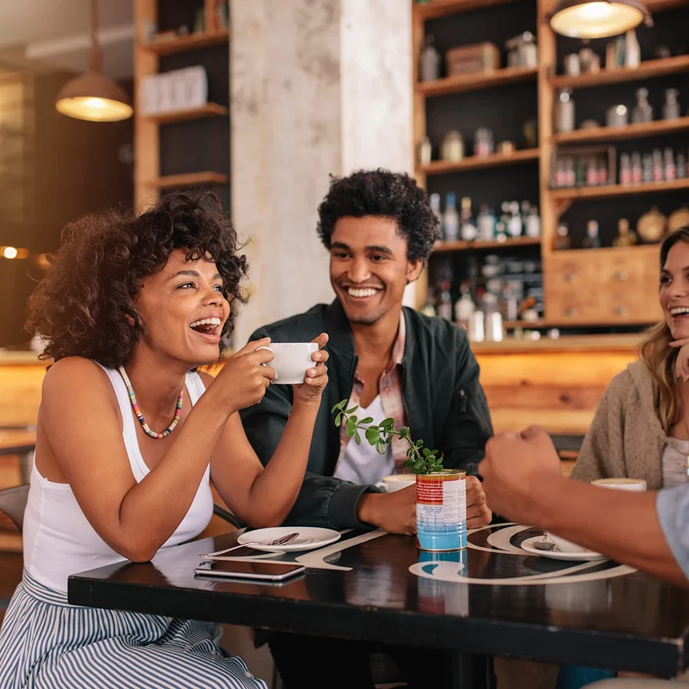 a young group of friends sit around a table drinking coffee and talking